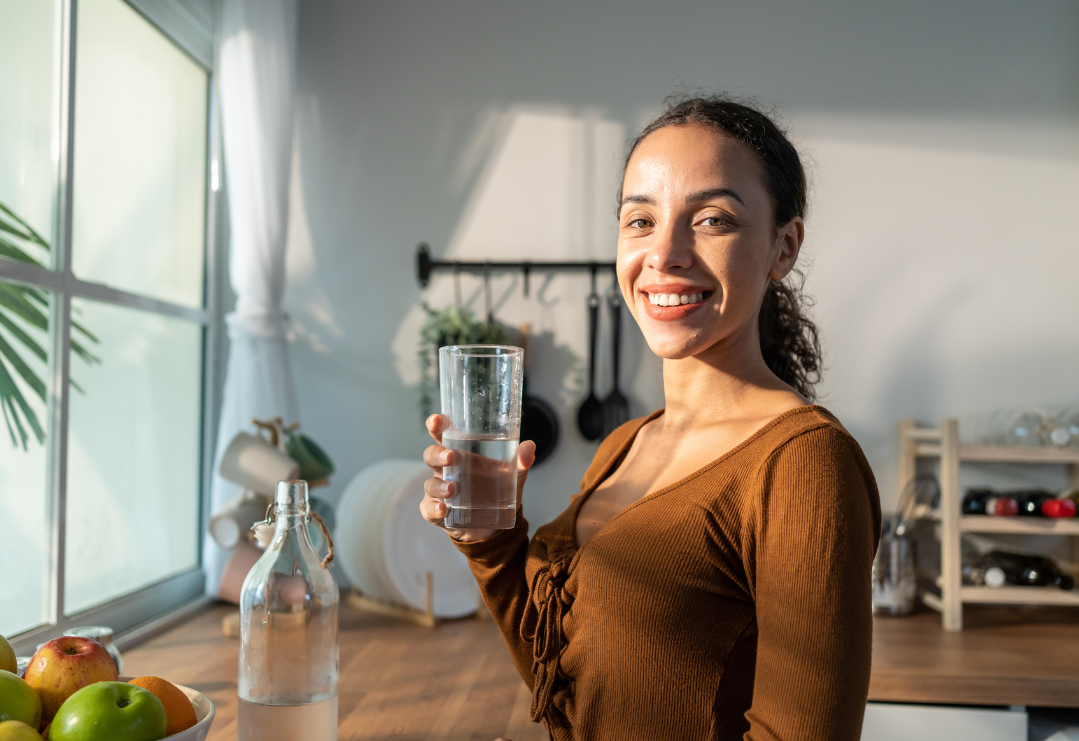 Young beautiful Latino woman holding clean water into glass in kitchen in house.